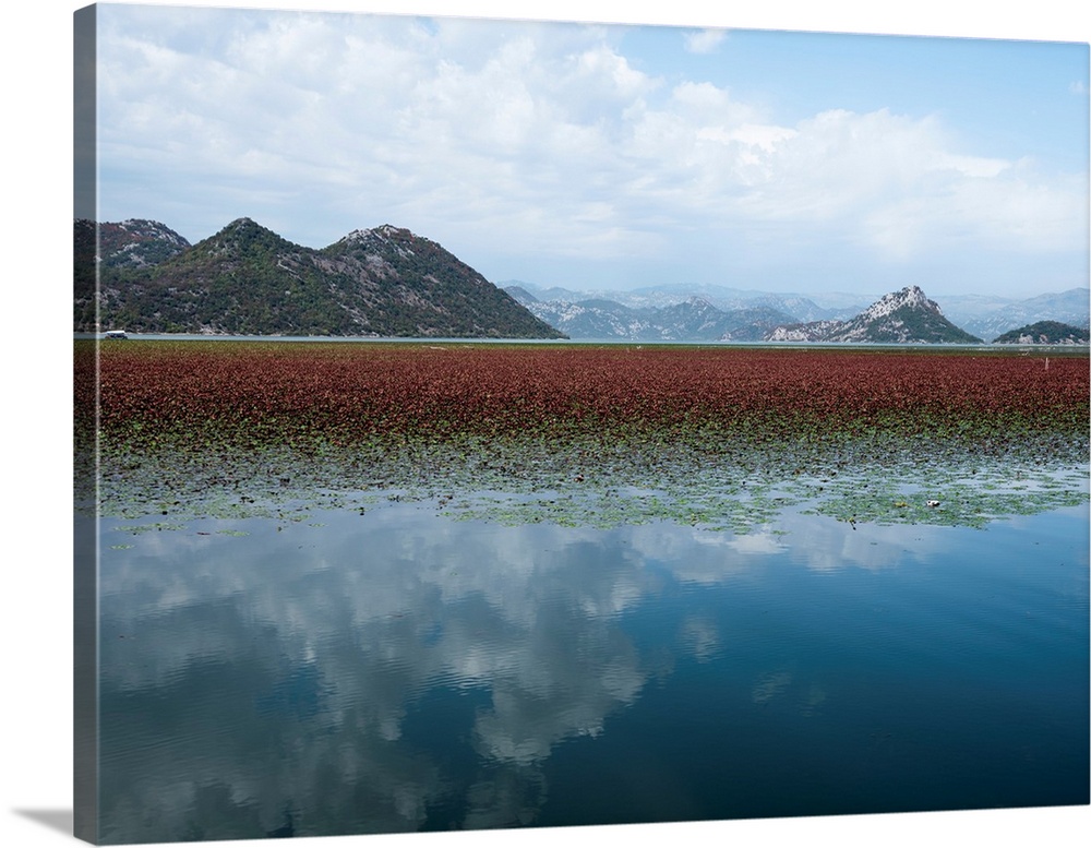 Photograph of a beautiful landscape with mountains and a lake that is reflecting the white clouds from the sky.