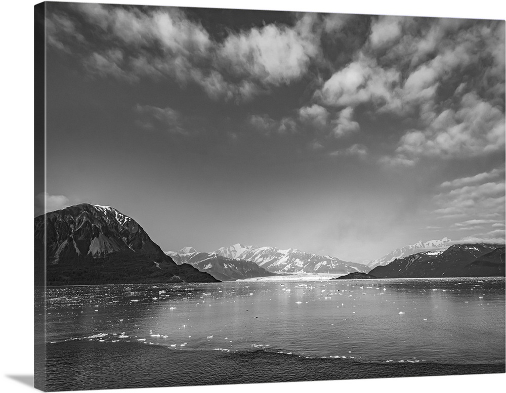 Luminous black and white image of glacier mountains rising around a glacier base surrounded by artic ocean under dramatic ...