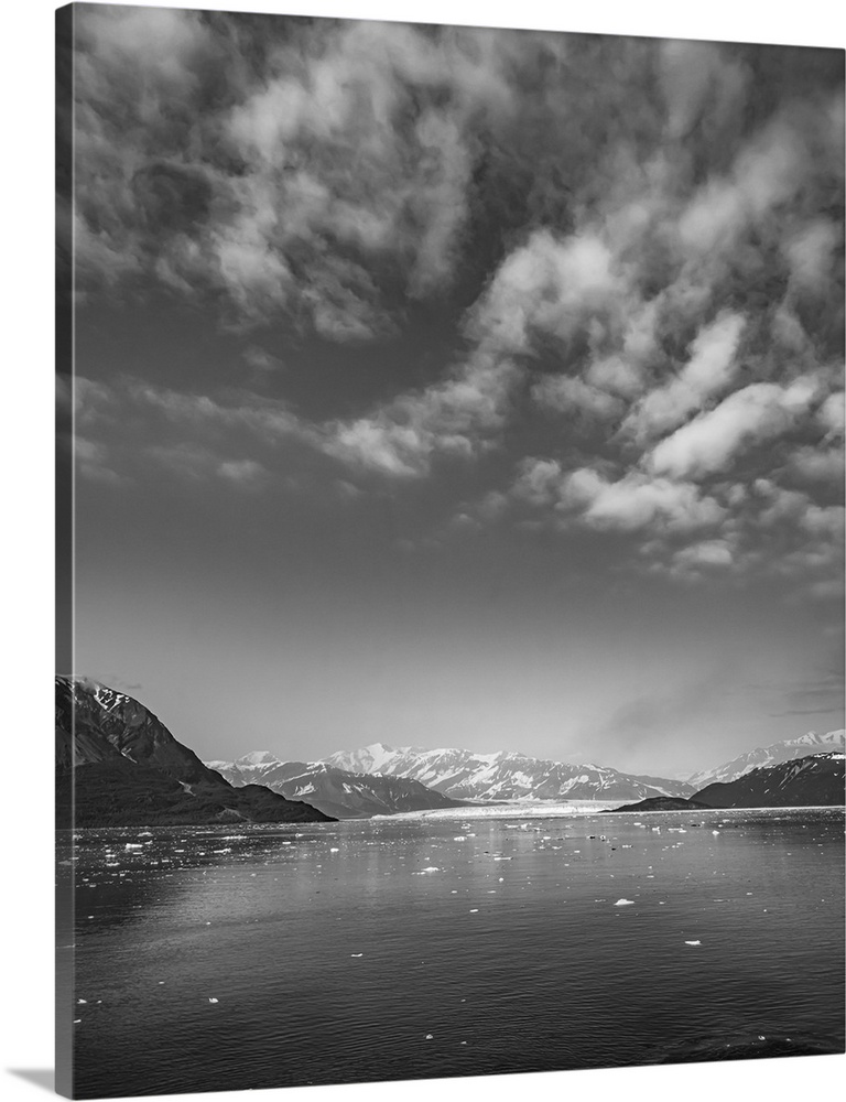 Luminous black and white image of glacier mountains rising around a glacier base surrounded by artic ocean under dramatic ...