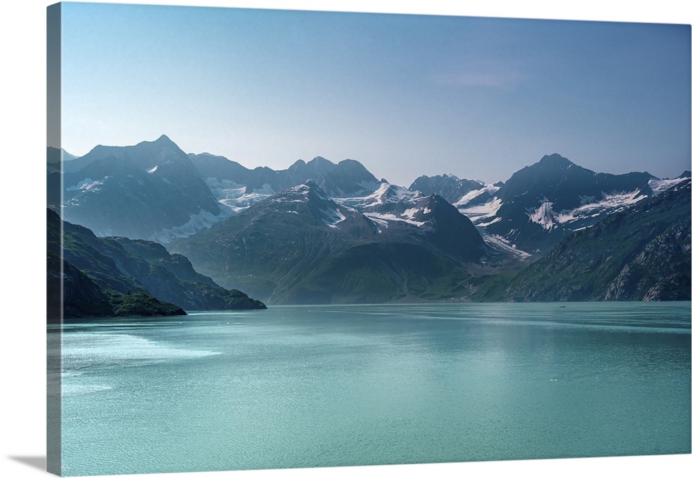 Beautiful Alaskan mid-morning scene of snow capped mountains rising out of luminous aquamarine blue glacier waters.