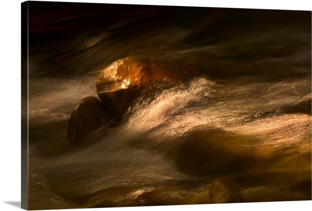 Photograph taken of rushing water gliding over rocks that are touched by spots of sunlight.