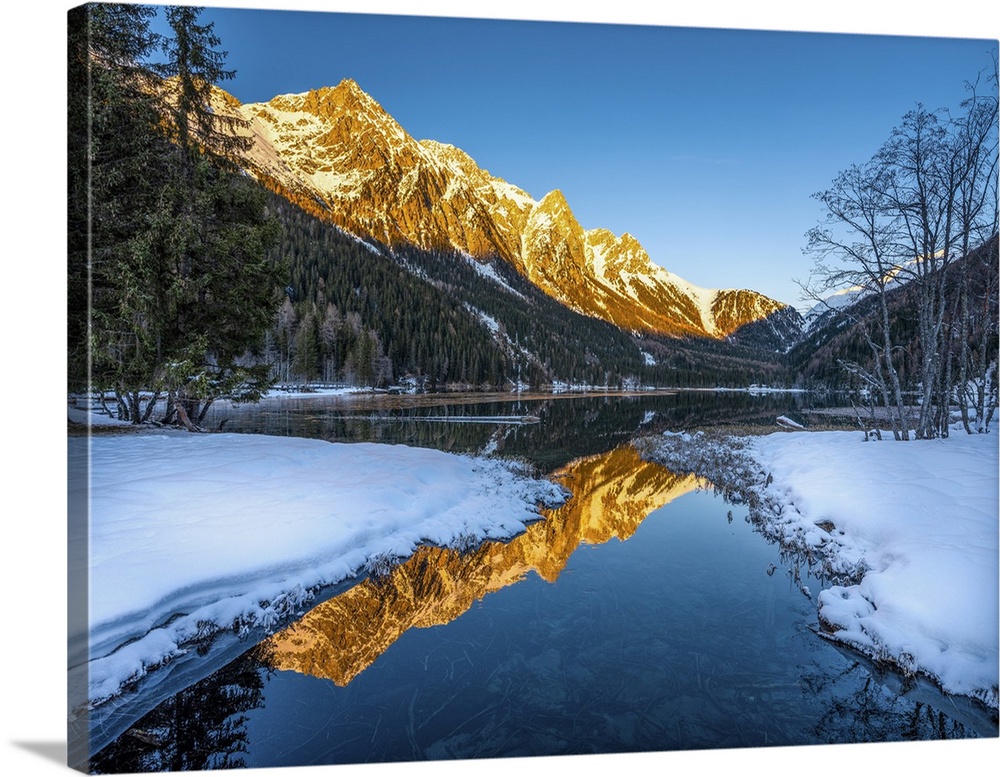 An alpine landscape in the middle of Lake Anterselva after a heavy snowfall. The sunset with its warm colors color the pea...