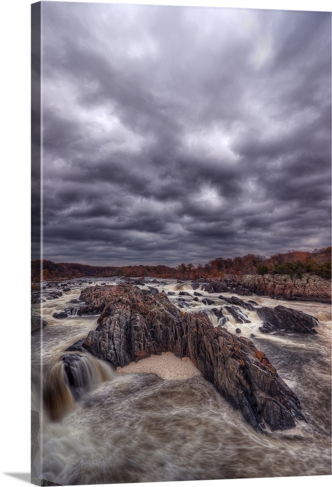 Very dark storm clouds over a rushing river lined with rocks.
