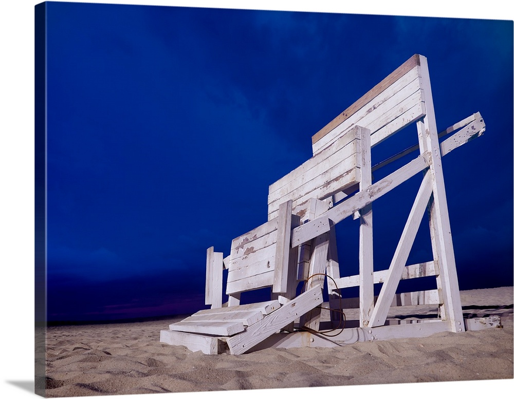 The remnants of a lifeguard tower on a sandy beach under a deep blue sky.