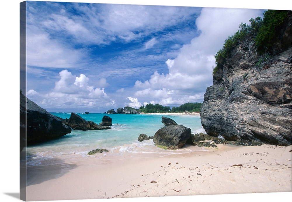 Big photograph displays a secluded portion of a sandy beach in Horseshoe Bay, Bermuda on a sunny day.  The rough and giant...