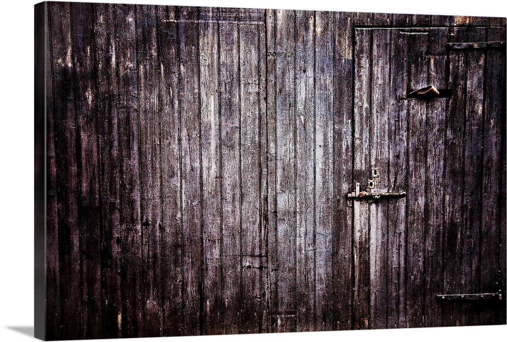 Large photograph focuses on the side of an aged wooden building with a couple concealed entrances.