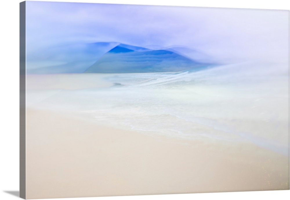 Abstract landscape photo with the ocean faintly washing up on a sandy shore and blue silhouetted mountains in the distance.