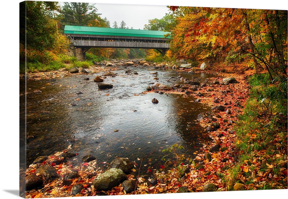 A covered bridge with a colorful roof stretching over the Ellis River in New Hampshire.