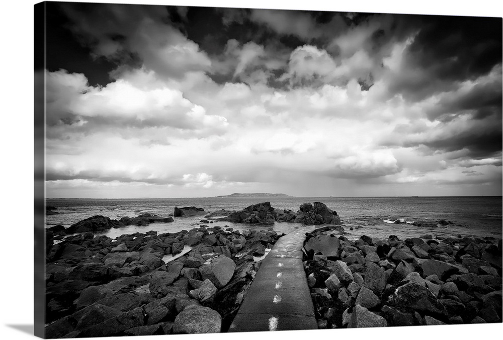 Black and white photograph of a road surrounded by coastal rocks leading into the ocean.