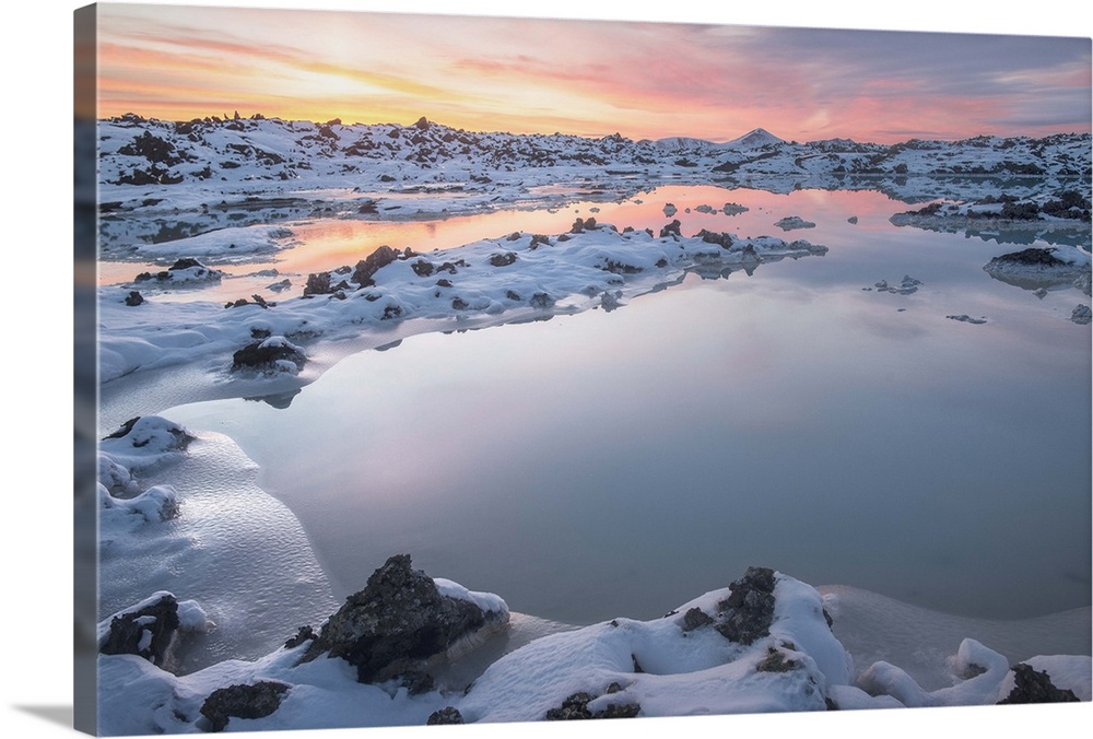 Snow covered rocks surround a calm pond at sunset, Iceland.