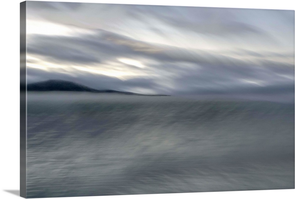 Blurred image of a lake with stormy skies above and a mountain in the distance.