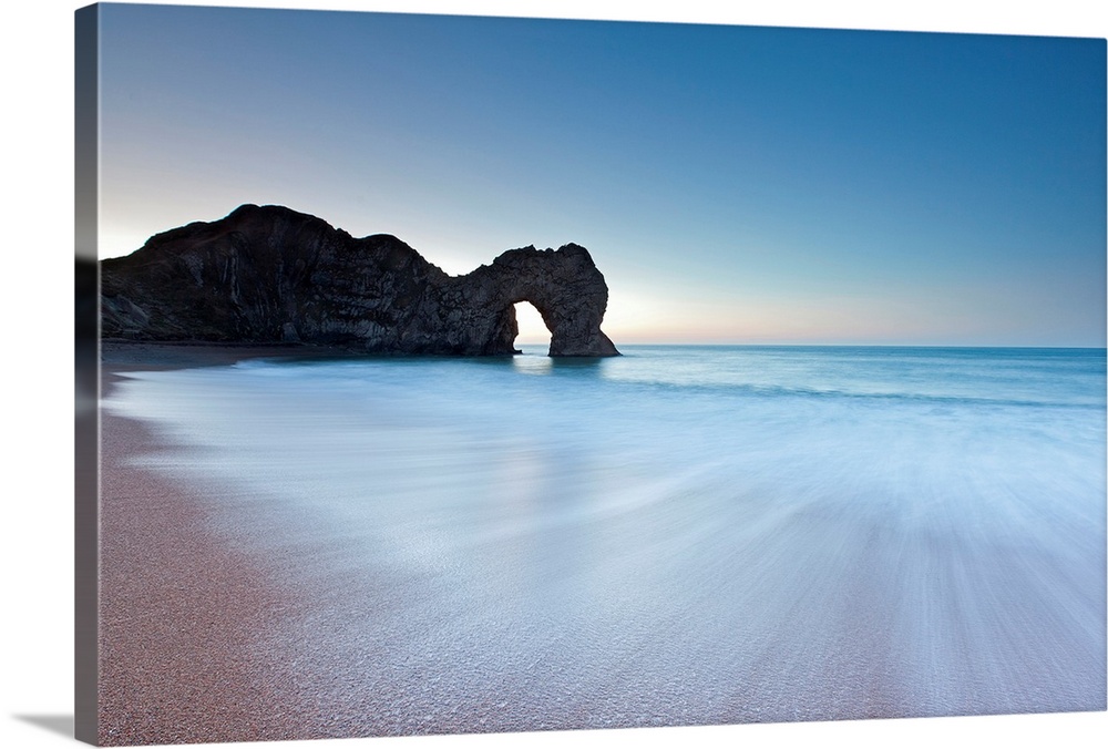 Durdle Door rock arch on the Dorset coast at sunrise with a blue sky and swooshing waves in minimalist energy.