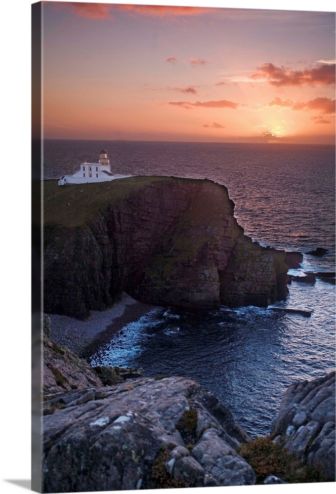 A sunset seascape over Neist Point Lighthouse, Isle of Skye, Scotland with a peach and gold sky.