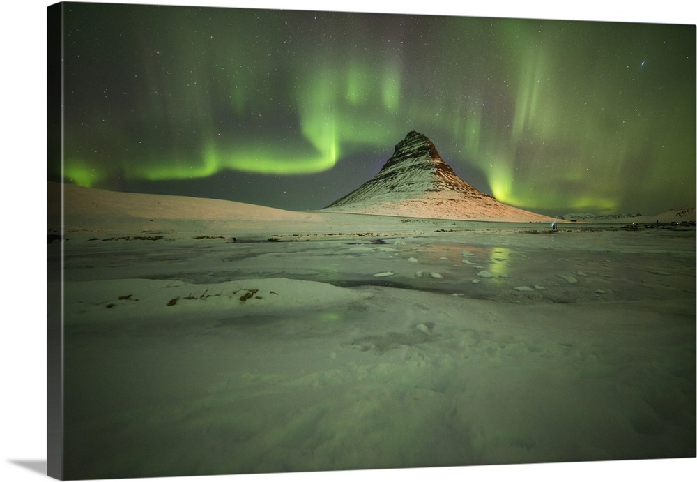 Green aurora borealis curling in the sky over Kirkjufell Mountain in Iceland.