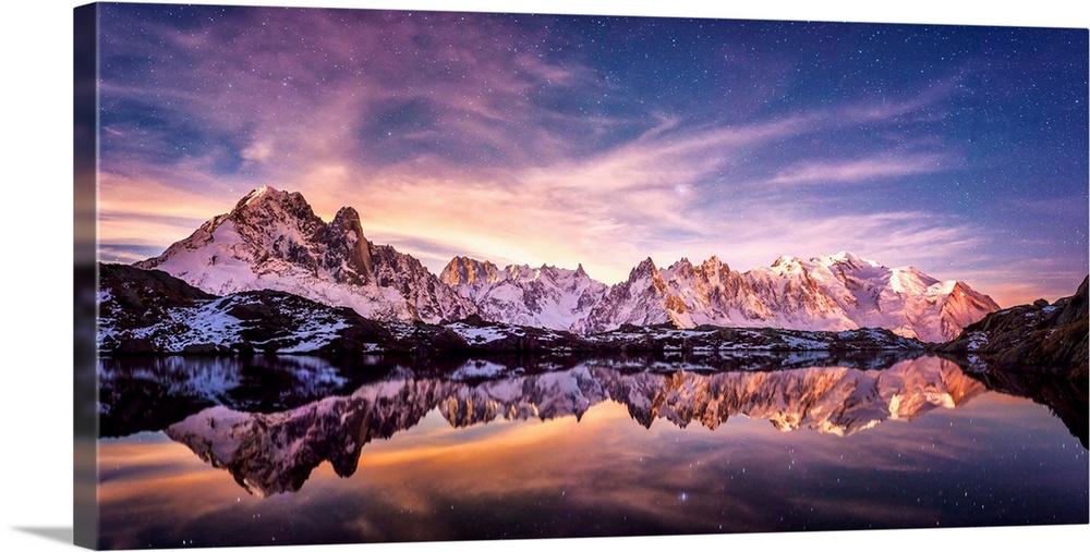 Fine art photograph of a snowy mountain range reflected in the water under a lavender sky in France.