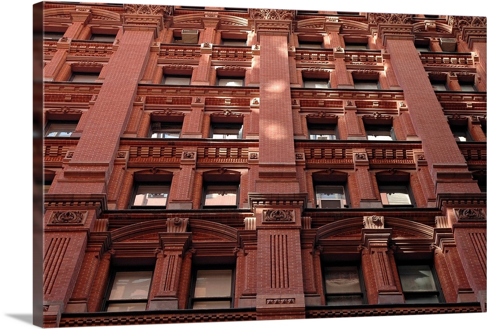 Looking up at the detailed architecture of a building with lots of brickwork, inset columns, and windows.