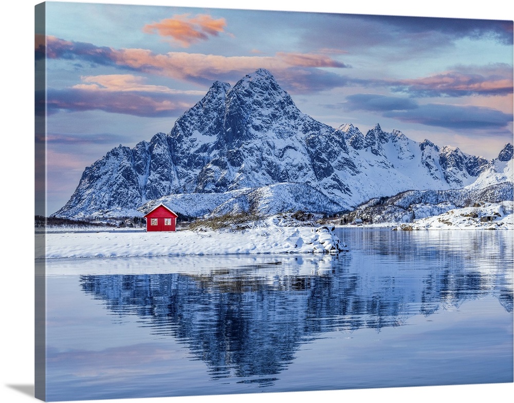 The Lofoten Islands offer spectacular scenery, a red house and the imposing snow-capped mountain behind which is reflected...