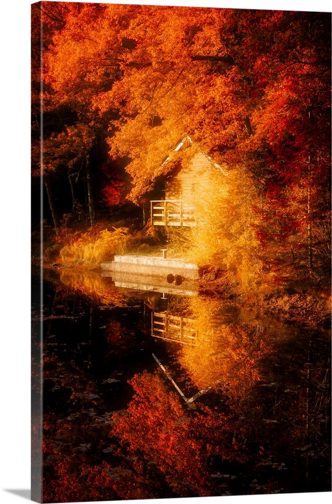 A small house at the edge of the water with deep orange leaves surrounding it.