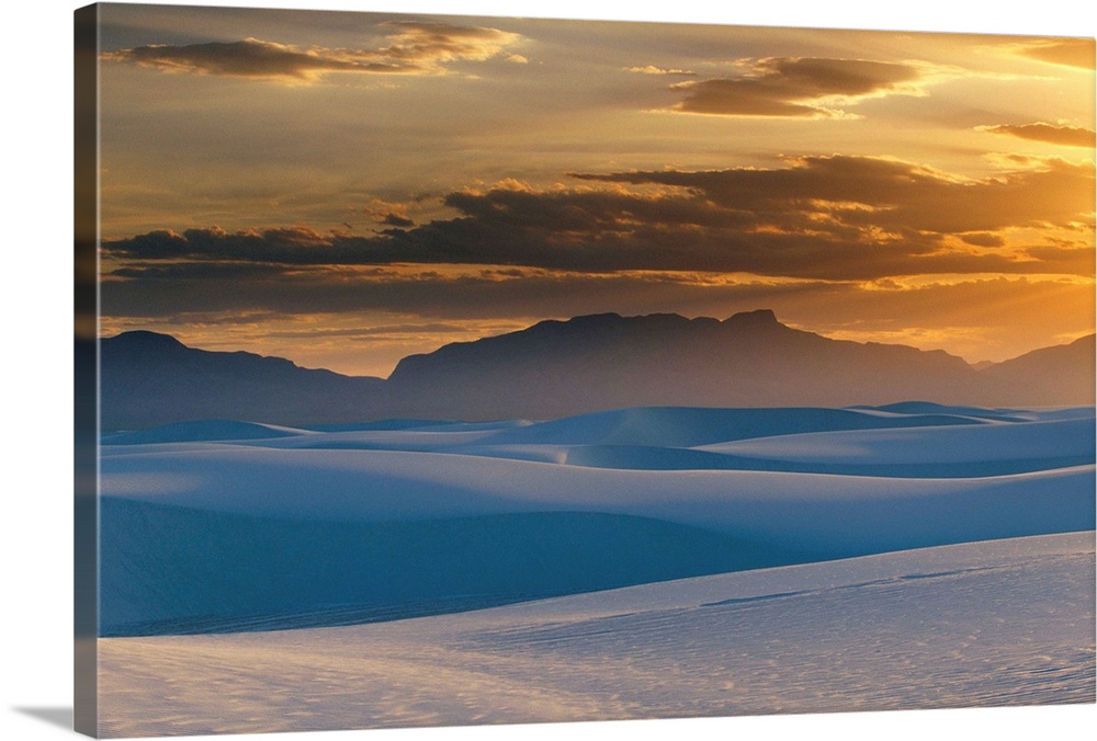 Large landscape photograph of the sun setting in a cloudy sky, over the Gypsum dunes, White Sands National Monument, in Ne...