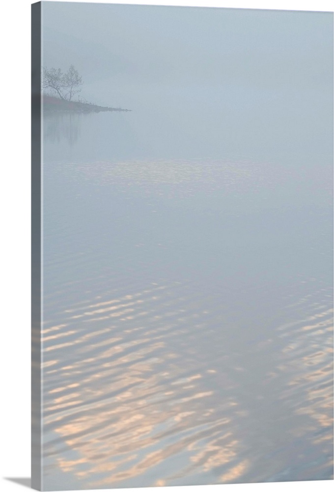 Fine art photo of a lake covered in fog in the morning, with a little bit of light reflecting off of it.