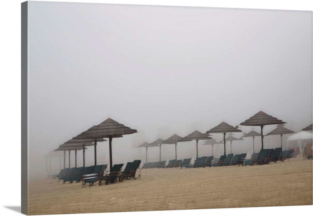 Blurred photograph of a sandy beach lined with beach chairs and umbrellas, created with multiple exposures.