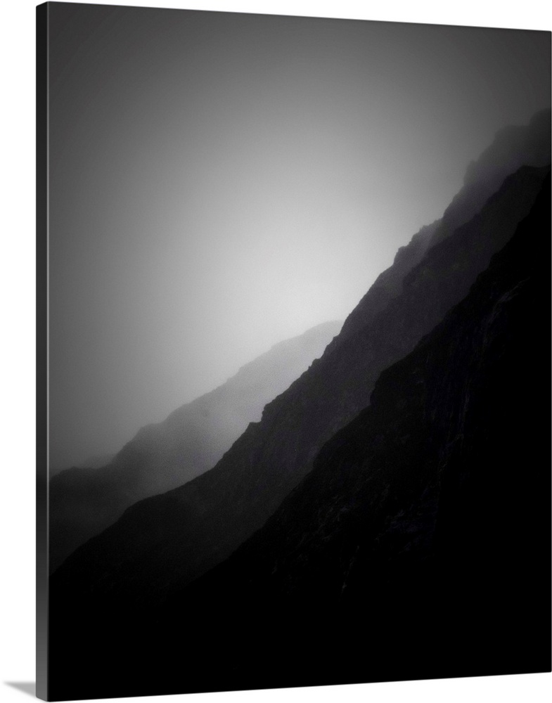 A black and white photograph of silhouetted mountain sides shrouded in haze.
