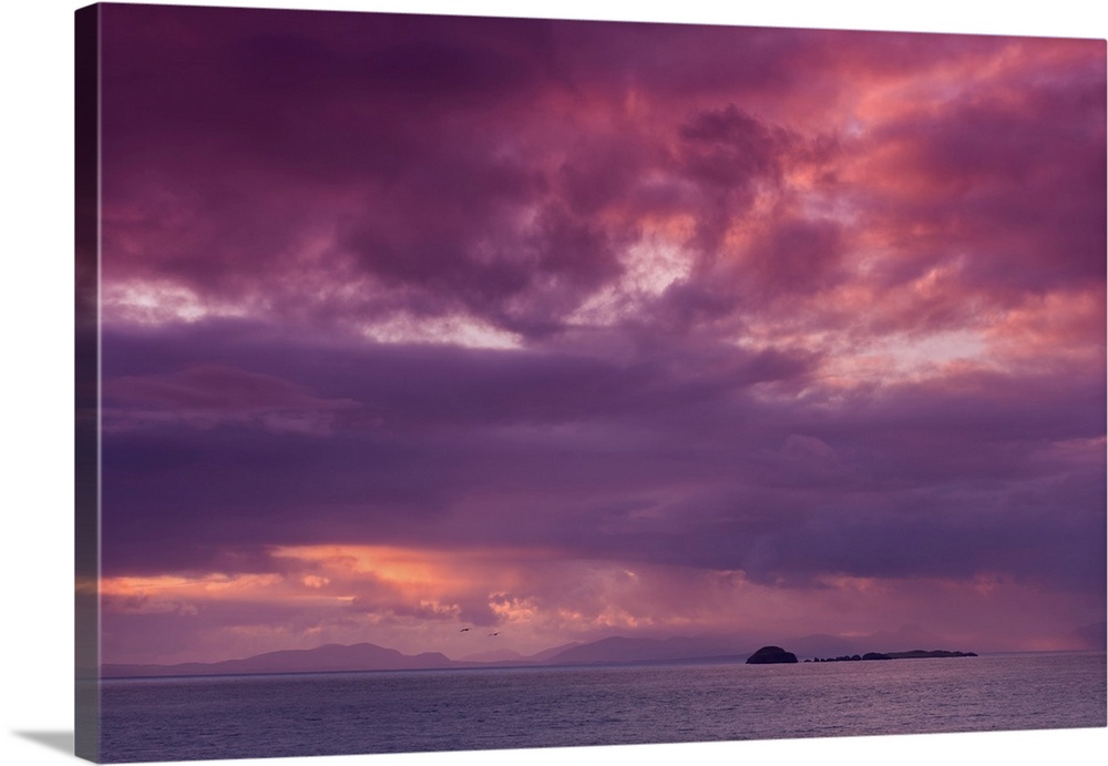 Fine art photo of a dramatic skyscape over a calm ocean with a small island in the distance.