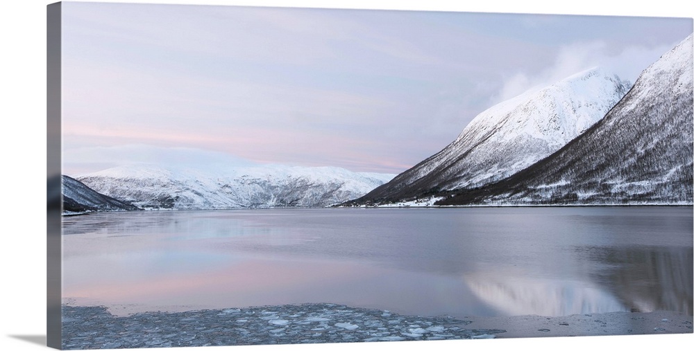 A tranquil cool pink blue mountainscape dawn in the Norweigian snow by a lake.