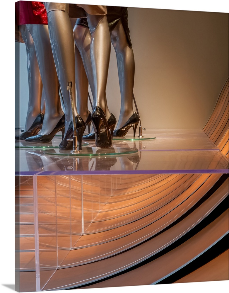 The legs of several bronze mannequin in the window of a designer store.