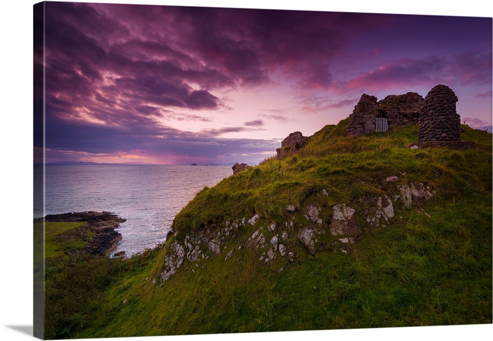 Fine art photo of grassy hills overlooking the sea under a pastel sky at dusk.