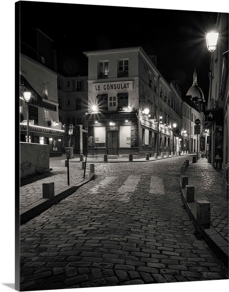 A nightscape in Monmarte, Paris, France showing the famous Le Consulat cafe with wrought iron street lamps and the cobbled...