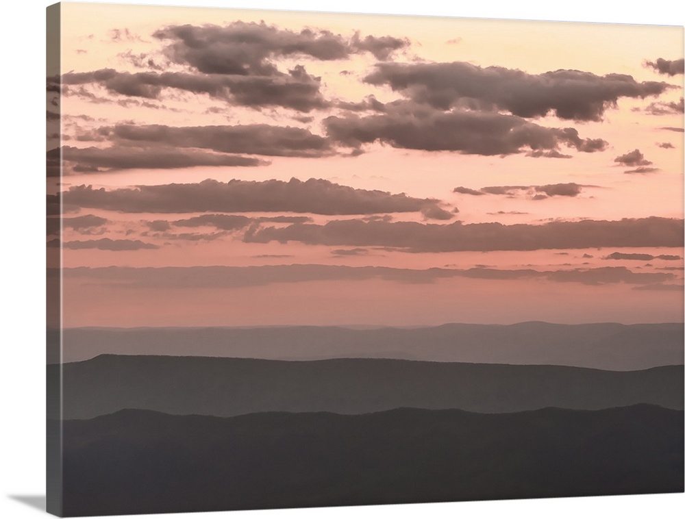 Pale pink cloudy sky over dark hills at twilight.