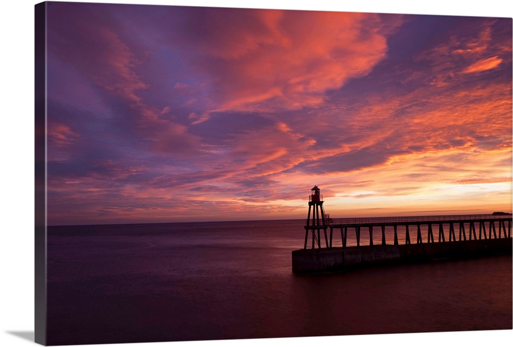 A dramatic peach, orange and red sunset over the lighthouse and pier at Whitby harbour, North Yorkshire, England.
