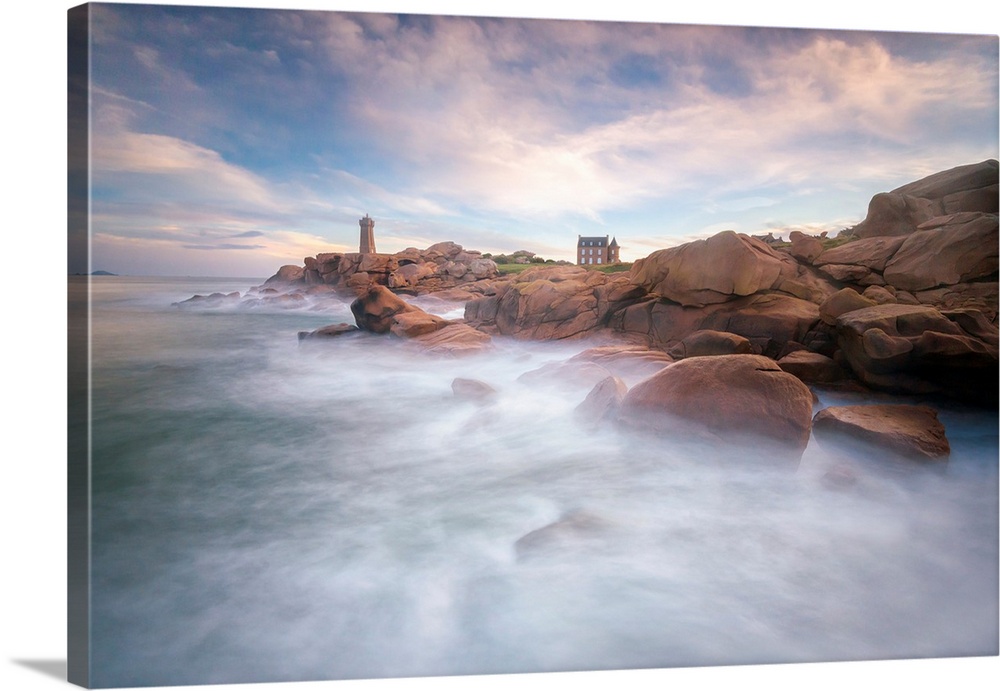 Fine art photo of misty ocean waters at the rocky coast of France with a lighthouse in the distance.