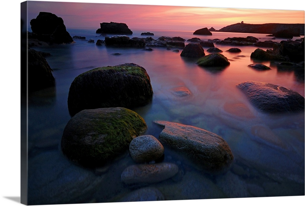 Rocky beach during pink sunset in Brittany, France, big rocks and quite sea at first plan.