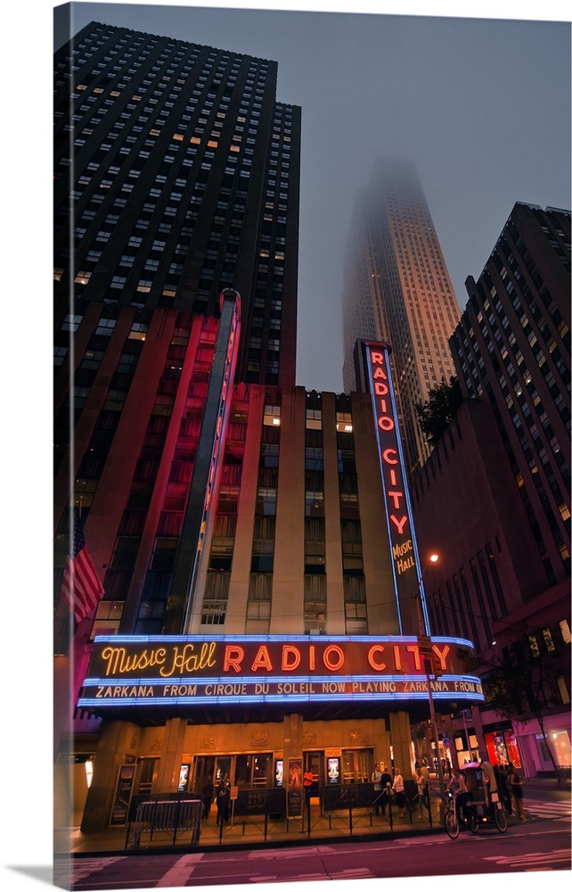Neon lights of Radio City Music Hall glowing in the evening under a foggy sky.