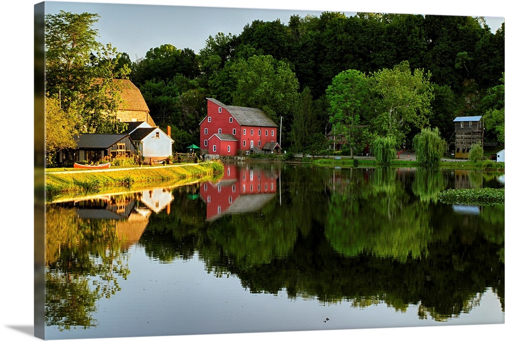 Fine art photo of a bright red house at the edge of a calm lake, with the reflection of the forest nearby.
