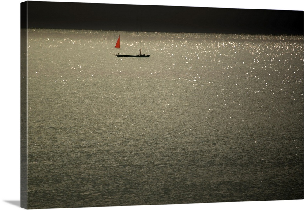Motion blurred image of a sparkling ocean with a small boat in the distance that has a red sail.