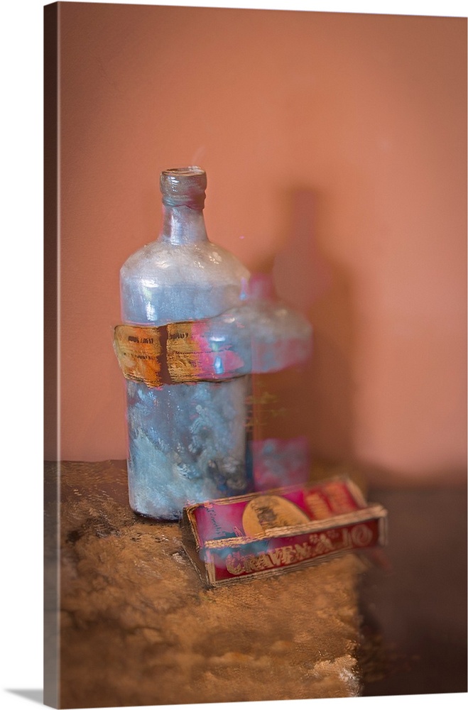 A distressed photo of a bottle and a box of cigarettes on textured table.