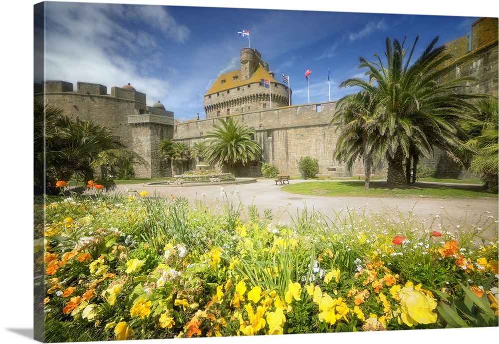 A historic castle in Brittany, France, surrounded by yellow flowers and palm trees.
