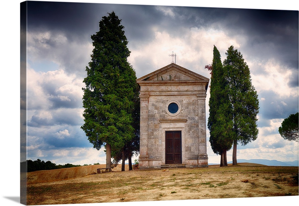 A photograph of a small chapel with a backdrop of a Tuscan landscape against rolling clouds.
