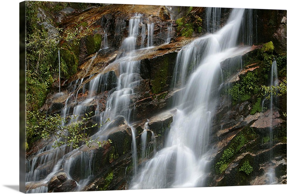 Giant horizontal photograph of small streams of water falling and flowing over a steeply sloped rocky surface, surrounded ...