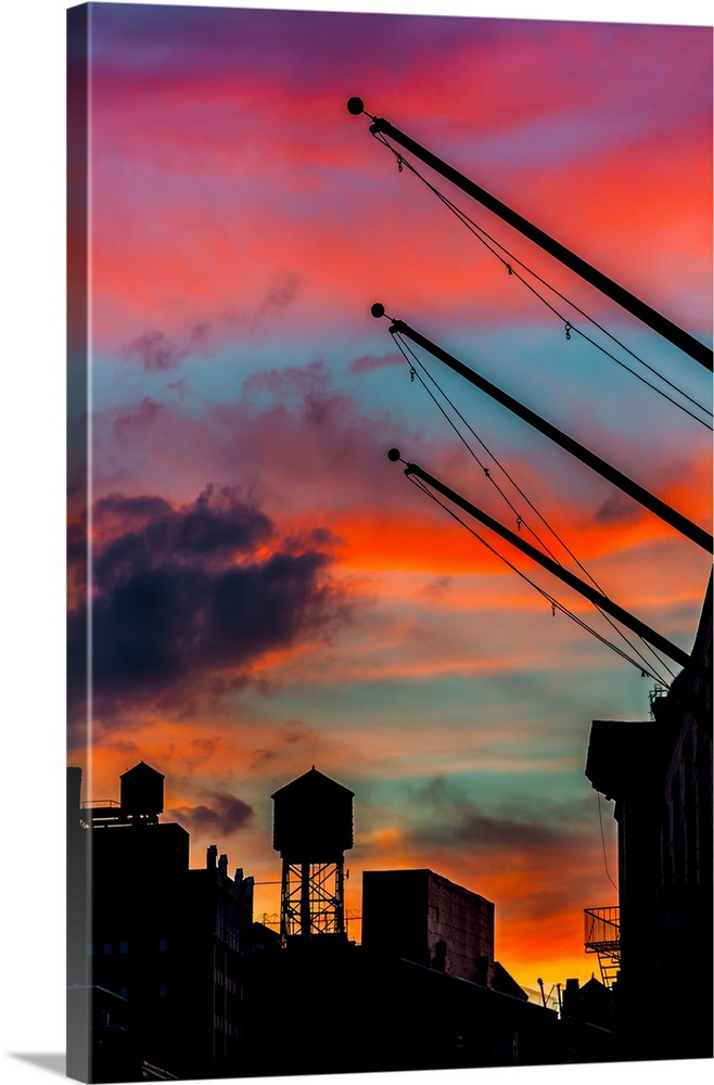 Silhouetted water tower and cranes against a vivid red and orange sunset sky.