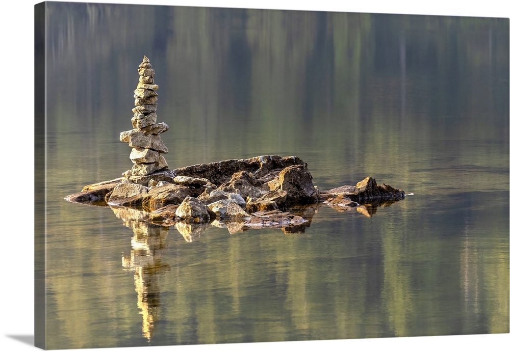 The early morning sun throws a beautiful warm side light on a small cairn in a shallow lake.