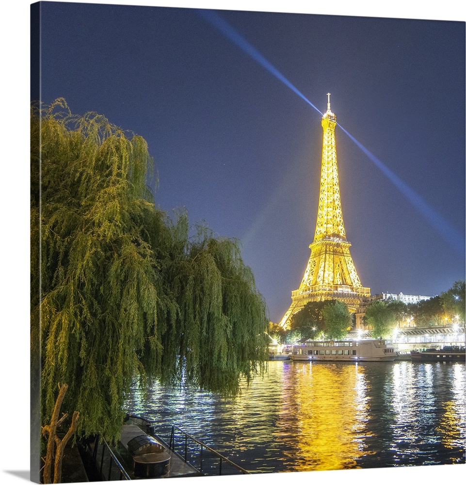 National french monument Eiffel tower lighting at night with boat on the Seine river with trees on the left side.