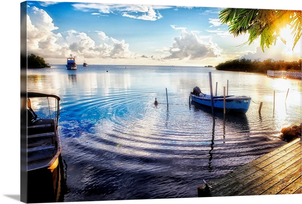Huge photograph includes a number of boats sitting within a bay of a tropical island as the sun begins to set.  One of the...