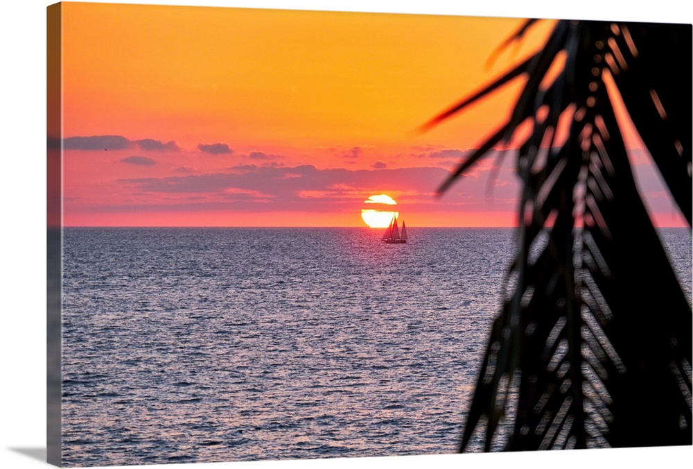 A photo of sun setting behind a boat on water in Puerto Vallarta, Mexico with a palm tree leaf on the right.
