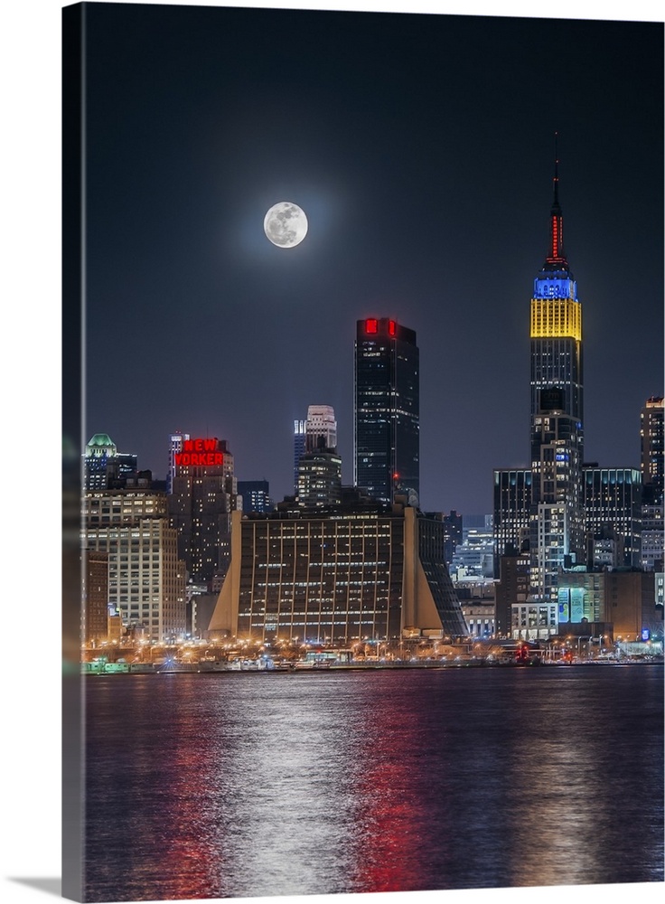 Large full moon shining over the Manhattan skyline, reflected in the bay below.