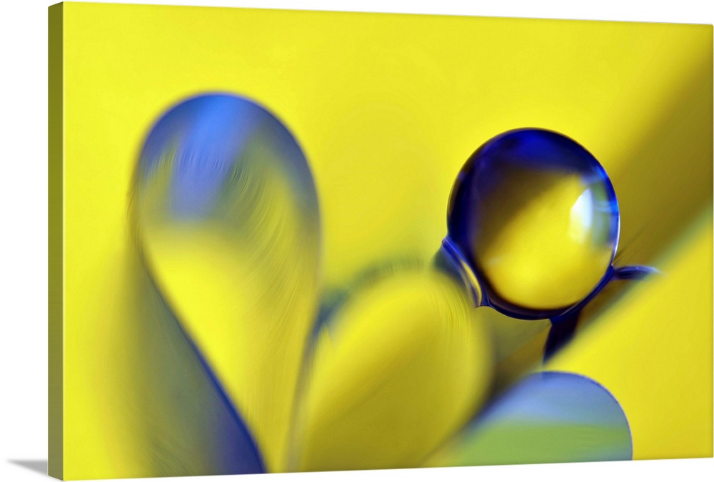 Macro abstract photograph of a water droplet reflecting on a yellow surface with blue ribbon-like designs below.