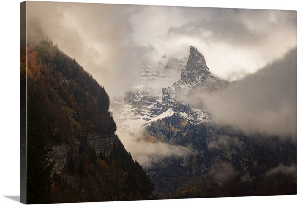 Place of Sixt-Fer-a-Cheval area in Savoie, France, big rocky mountain with snow going throw the fog at fall with colored t...